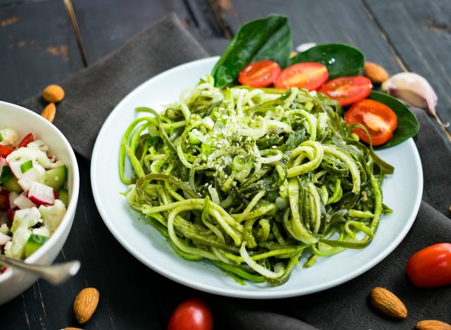 Zucchini raw vegan pasta with avocado dip sauce, spinach leaves and cherry tomatoes on plate. On dark background. Vegetarian healthy food
