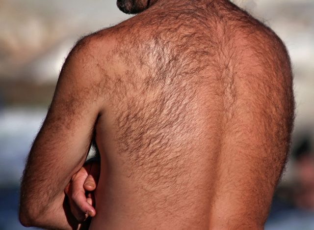 man with a very hairy back standing outside by a river on a hot summer day