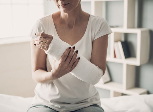 Close-up of Female Broken Arm in Plaster Cast. Caucasian Injured Woman in White T-Shirt Sitting and Holding Wrist in Gypsum Bandage with Physical Pain in Fractured Bone. Health Care concept