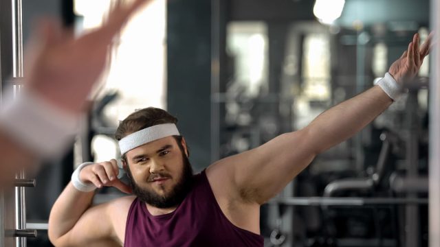 Trendy fat man showing dab move at mirror, satisfied with weight loss results