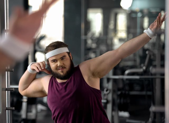 Trendy fat man showing dab move at mirror, satisfied with weight loss results