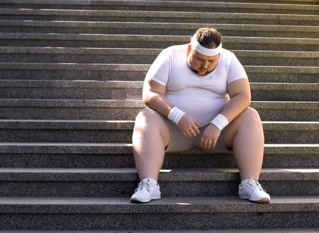 Fat man sitting on stairs after jogging, no faith in himself, insecurities