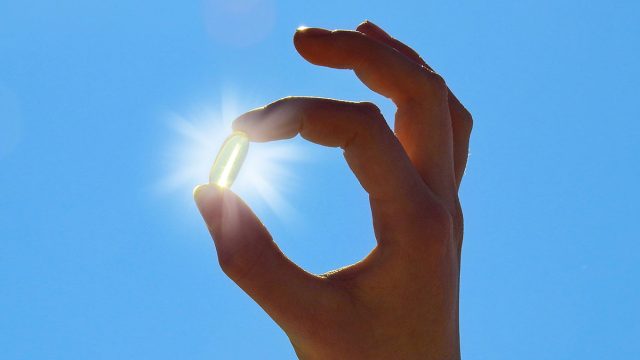 Young Woman is holding Vitamin D Capsule. Sun and blue Sky.
