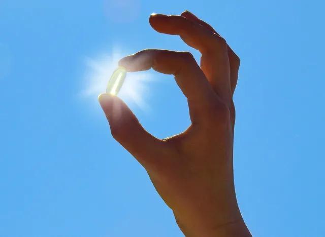 Young Woman is holding Vitamin D Capsule. Sun and blue Sky.