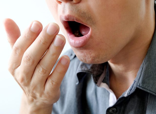 A man checks for bad breath and breathes with his hands. he has bad breath Concept of oral and dental health