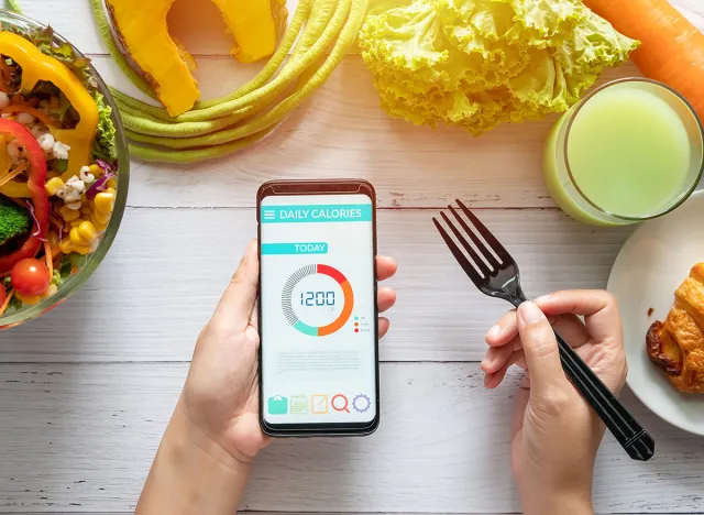 Calories counting , diet , food control and weight loss concept. woman using Calorie counter application on her smartphone at dining table with salad, fruit juice, bread and vegetable