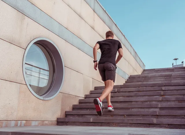 A male athlete, a view from back, runs in morning on a run on stairs, in summer in city. Sportswear T-shirt shorts. Fitness, youth lifestyle, healthy lifestyle in the city. Free space for text