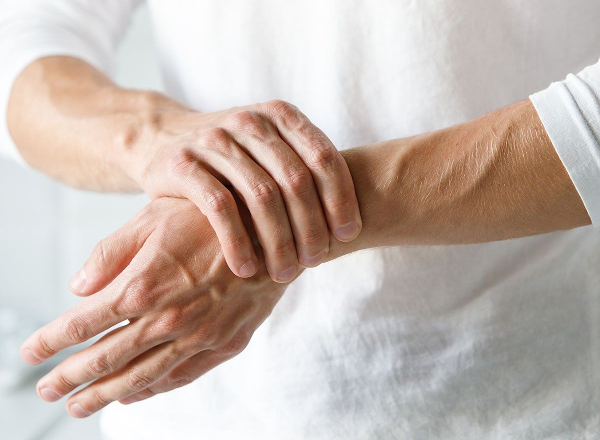 Closeup of male arms holding his painful wrist caused by prolonged work on the computer, laptop. Carpal tunnel syndrome, arthritis, neurological disease concept. Numbness of the hand