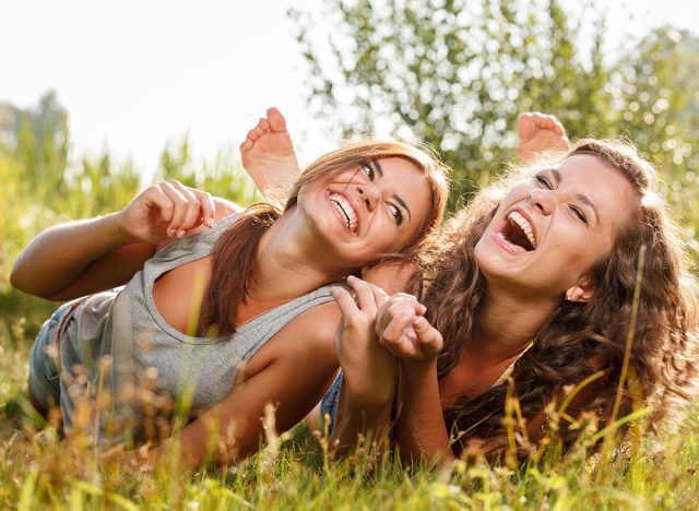 two girlfriends in T-shirts lying down on grass laughing having good time