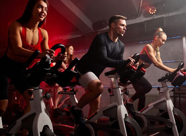 people biking in spinning class at modern gym, exercising on stationary bike. group of caucasian people athletes training on exercise bike