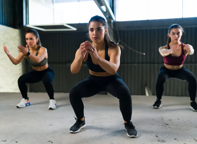 Beautiful women doing a cardio HIIT routine and squatting. Three fit women in sportswear working out and doing squats in the gym