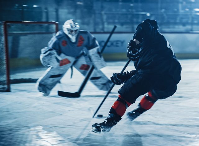 Ice Hockey Arena: Professional Forward Player Breaks Defense, Prepairing to Shot Puck with Stick to Score Goal. Two Competitive Teams Play Intense Game.