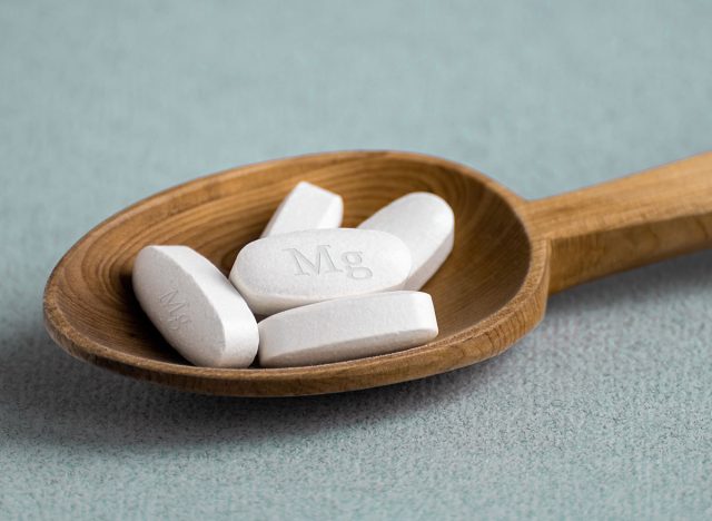 Tablets , vitamins with the abbreviation Mg ( magnesia, the macronutrient magnesium ) lying in a wooden spoon on a light background. Copy space.