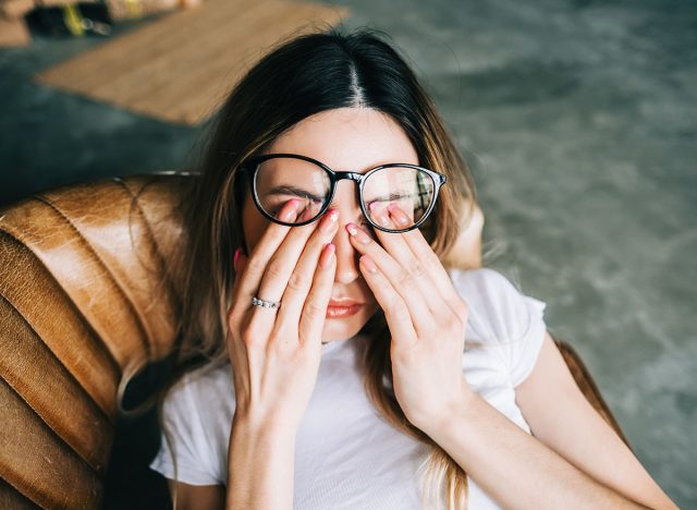 Young woman rubs her eyes after using glasses. Eye pain or fatigue concept.