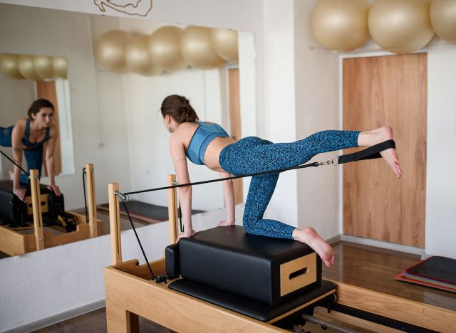 A young woman in sportswear does Pilates on a reformer, lifting her leg up.Side view.Pilates, a pilates reformer class.Healthy Lifestyle Concept.High quality photo