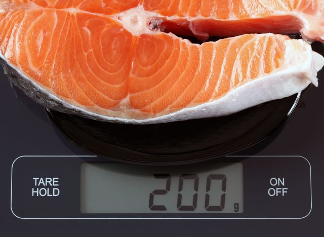 Steak of salmon fish in a black plate on digital scale displaying 200 gram.