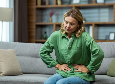 An elderly woman is sitting on the sofa at home, holding her stomach with her hands. Feels the pain of internal organs, indigestion, poisoning, menstrual pain.