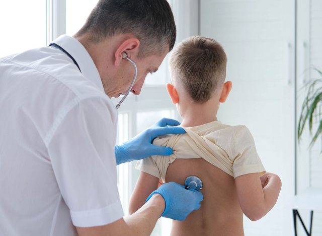 The doctor listens to the breathing of a little boy through a stethoscope. Pediatrician with stethoscope listens to the lungs of a child with bronchitis and cough