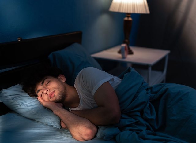 Peaceful young man sleeping in a comfortable bed alone at home, enjoying his orthopedic mattress and cozy pillow. Good sleep concept. Copy space