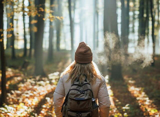 Foggy cold morning weather in autumn. Woman with backpack and knit hat hiking in forest at fall season