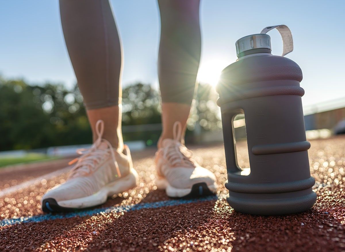 Close-up of a large water bottle on a running track with woman's legs in background