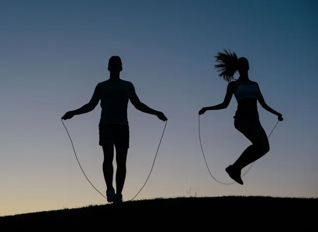Guy with girl warming up on a skipping rope before the competition. Jumping on the a skipping rope outdoors. Sport workout outdoors. Athletics.