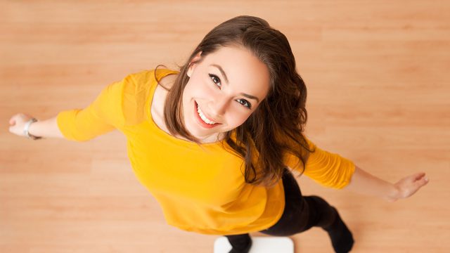 Portrait of young brunette beauty using household scale.