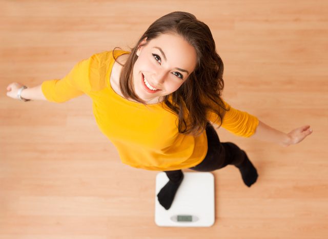 Portrait of young brunette beauty using household scale.