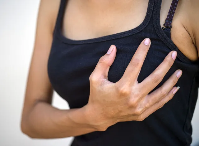 Closeup cropped portrait young woman with breast pain touching chest, selective focus