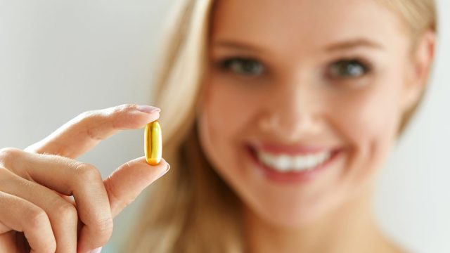Vitamin And Supplement. Beautiful Smiling Woman Holding Fish Oil Capsule In Hand. Portrait Of Happy Girl Taking Pill With Cod Liver Oil, Omega-3. Diet Nutrition And Healthy Eating Lifestyle Concept.