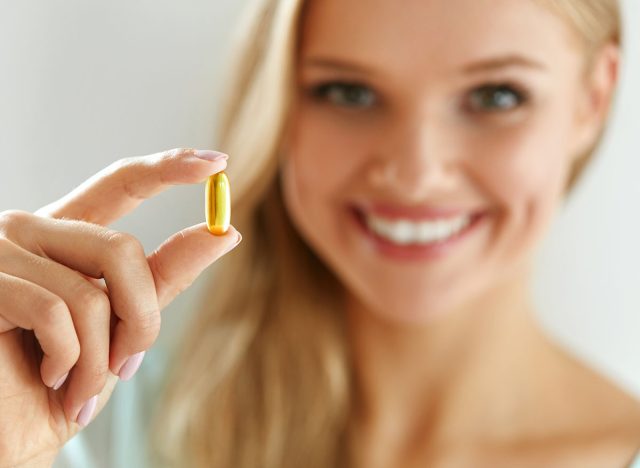 Vitamin And Supplement. Beautiful Smiling Woman Holding Fish Oil Capsule In Hand. Portrait Of Happy Girl Taking Pill With Cod Liver Oil, Omega-3. Diet Nutrition And Healthy Eating Lifestyle Concept.