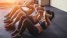Group of athletic adult men and women performing sit up exercises to strengthen their core abdominal muscles at fitness training