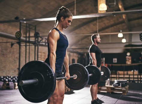Strong woman and man holding heavy barbells in gym. Horizontal indoors shot