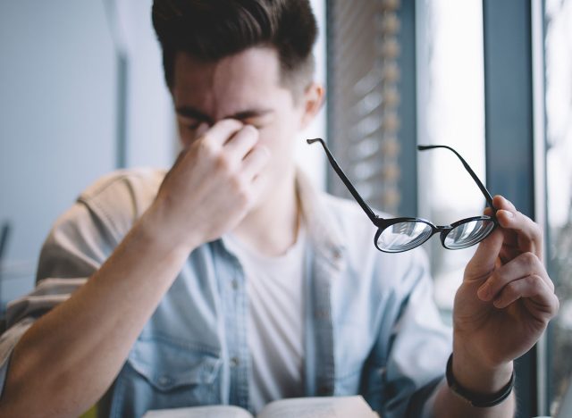 Close up portrait of an attractive man with eyeglasses. Poor young guy has eyesight problems. He is rubbing his nose and eyes because of weariness