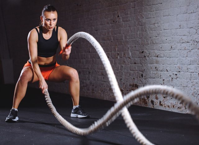 Woman training with battle rope in cross fit gym