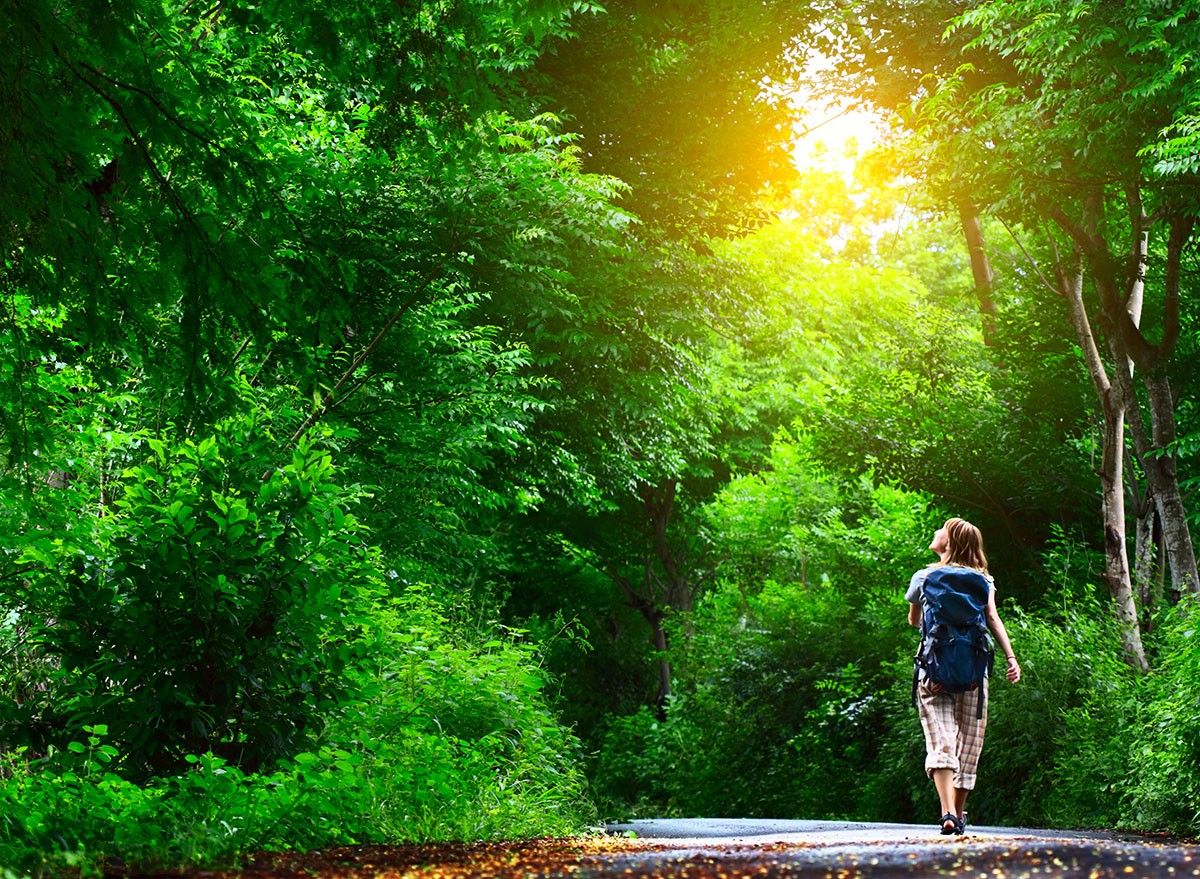 Young woman walking on green asphalt road in forest