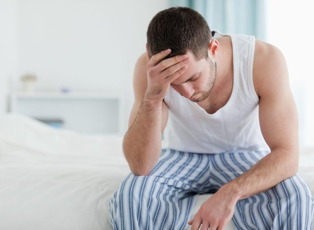 Ill man sitting on his bed with his head on his hand