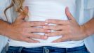 woman clutching her stomach with her hands in discomfort