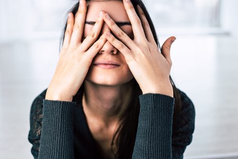 Dark-haired girl covers her face with hands