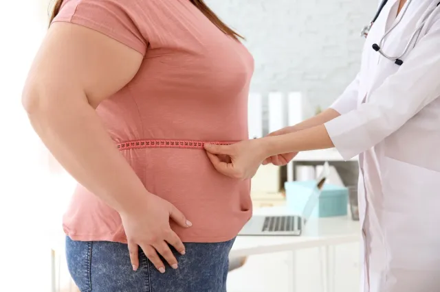 Female doctor measuring waist of overweight woman with measuring tape in clinic