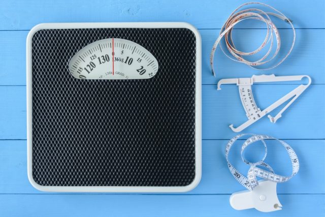 Mechanical weight scale, body mass control concept : Bathroom scale, personal accurate body fat tester / skin fold caliper measurement tool for stomach / belly and measuring tape on blue background