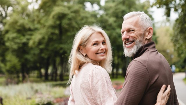 Smiling happy caucasian mature spouses hugging embracing while walking on a date in park together. Bonding, love and relationship