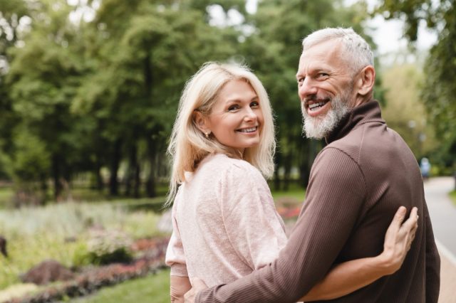 Smiling happy caucasian mature spouses hugging embracing while walking on a date in park together. Bonding, love and relationship