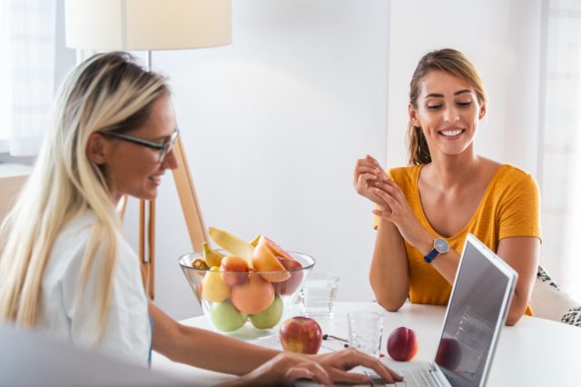 Doctor nutritionist, dietician and female patient on consultation in the office. young smiling female nutritionist in the consultation room. Nutritionist desk with healthy fruit and measuring tape.