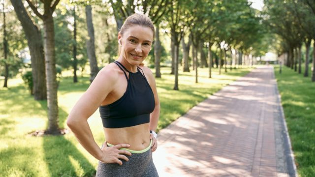 Sporty mature woman in sportswear and earphones looking at camera while jogging in a green park on a sunny summer day
