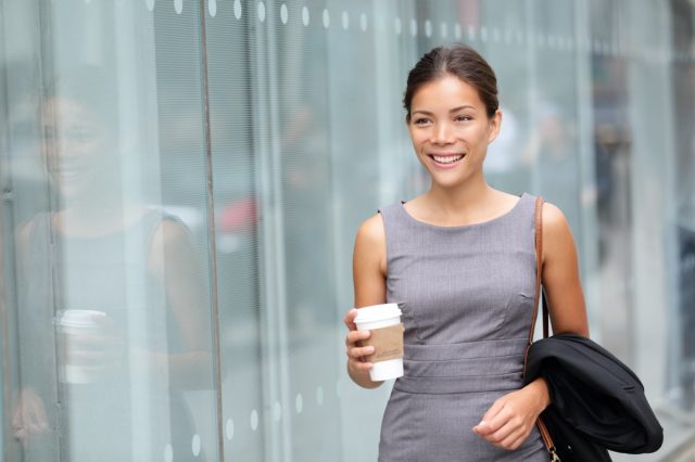 Business woman walking drinking coffee. Lawyer professional or similar walking outdoors happy holding disposable paper cup. Multiracial Asian / Caucasian businesswoman smiling happy outside.