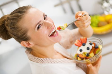 Happy young woman eating fruits salad.