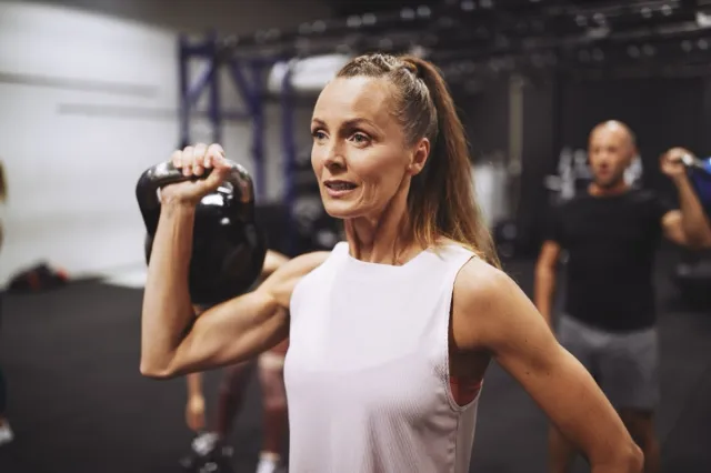 Fit mature woman in sportswear lifting a dumbbell during a strength training session at the gym