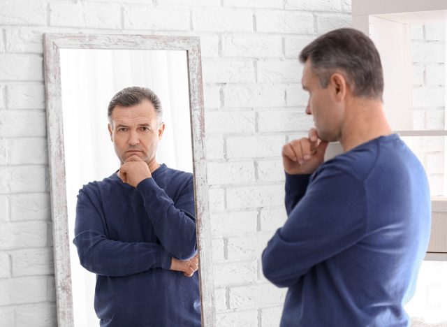 Thoughtful mature man standing near mirror at home