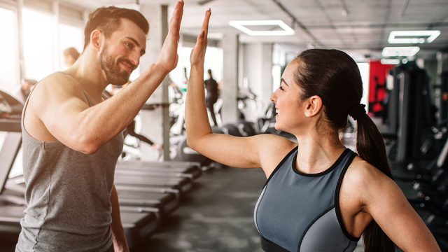 A beautiful girl and her well-built boyfriend are greeting each other with a high-five. They are happy to see each othr in the gym. Young people are ready to start their workout.